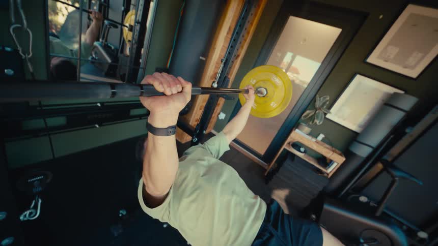 A unique point-of-view shot from the barbell shows a strong man performing a bench press workout in his home gym