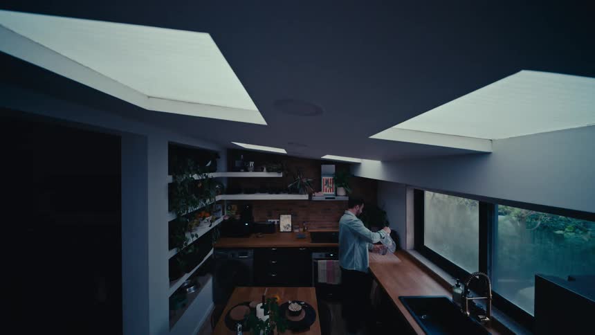 A man enjoys a peaceful morning routine, drinking coffee by the window in a modern kitchen with skylights
