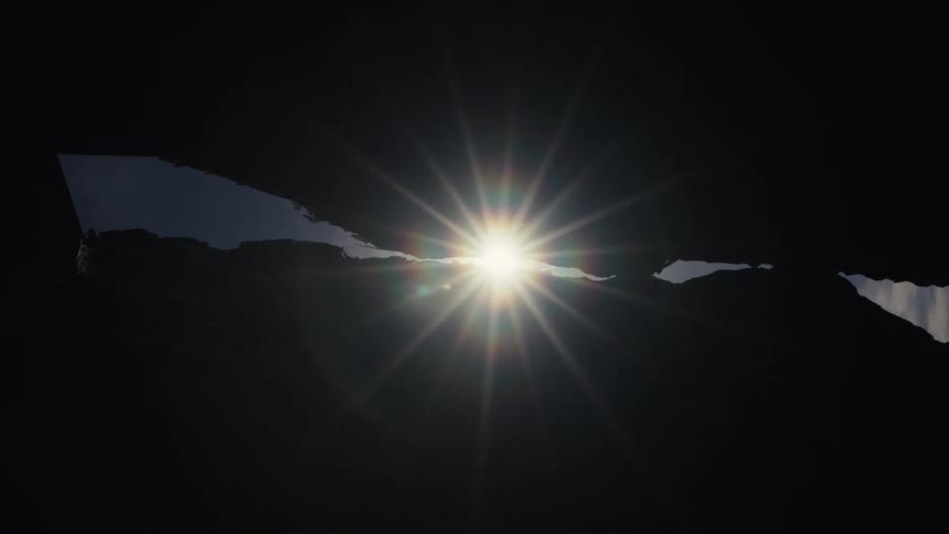A brilliant sun starburst slowly emerges through a dark, silhouetted crevice creating a lens flare
