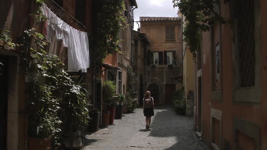 A young woman in a backpack walks in between buildings in the mediterranean town