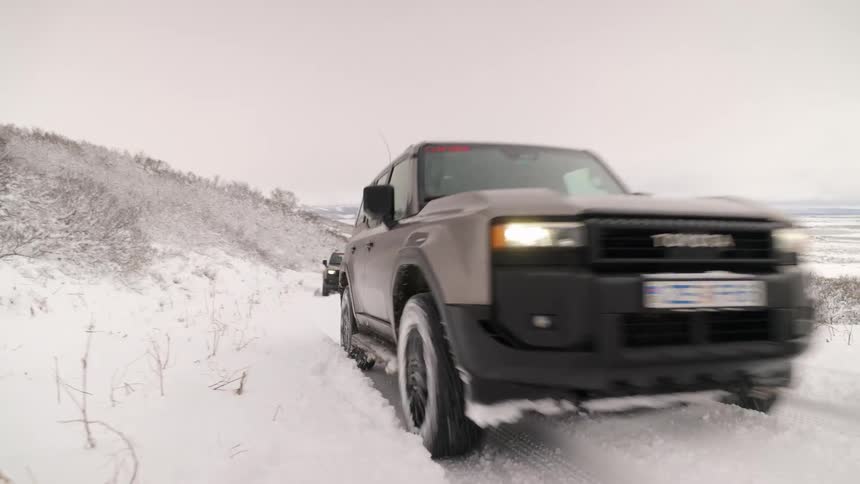 A silver Toyota SUV drives on a remote, snow-covered road through a vast winter landscape