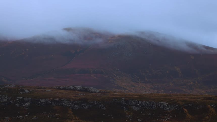 Misty clouds gracefully glide over the peaks of a remote, colorful mountain landscape