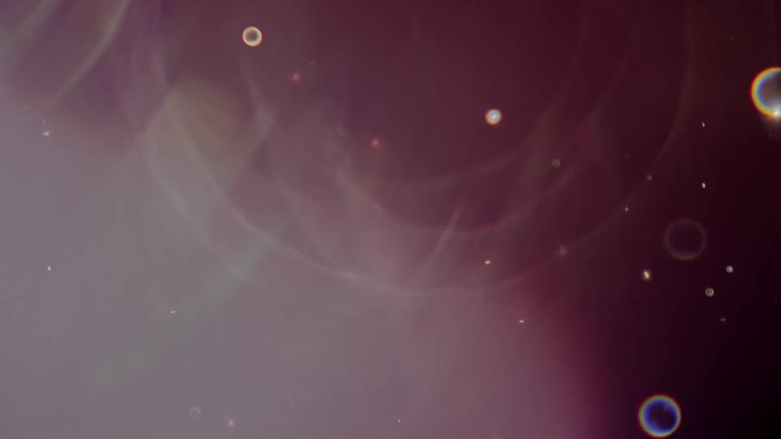 Colorful abstract light flares and cosmic particles drift slowly through a dark, dreamlike space