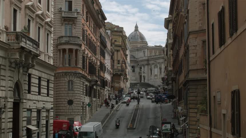 Scooters and cars travel down the steep road in the city