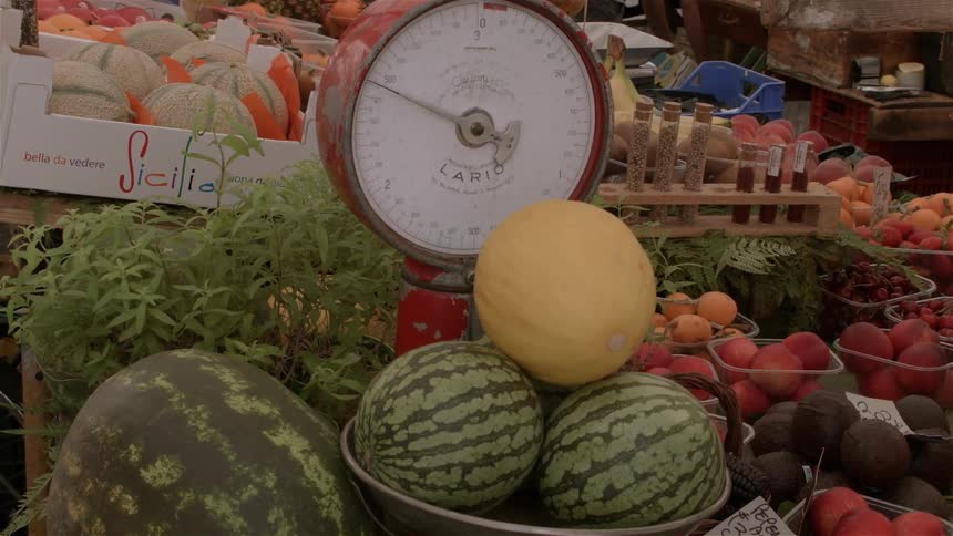 Melons sit in a scale at an outdoor market