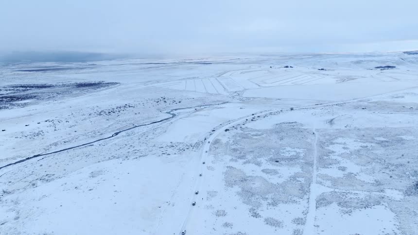 High aerial drone view of a convoy of vehicles on an expedition across a vast, desolate, snow-covered landscape