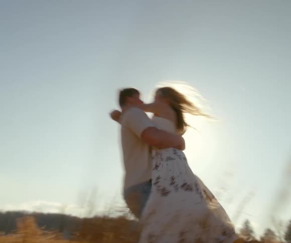 A dreamy, slow-motion shot of a man lifting and spinning a woman in a romantic embrace in a sunlit field of tall grass
