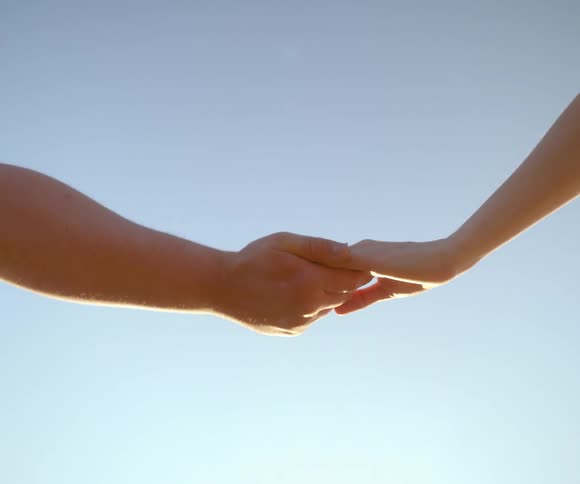A close-up of a man's and a woman's hands gently holding and then letting go against the sunlit blue sky