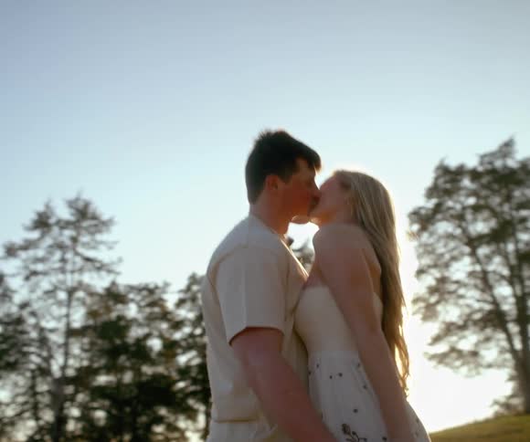 A loving young couple twirls in a sun-drenched field before stopping to share a romantic kiss in slow motion