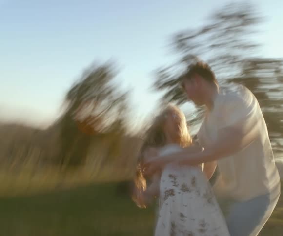 A blurry, dreamlike shot of a joyful couple spinning and dancing together in a sun-drenched field
