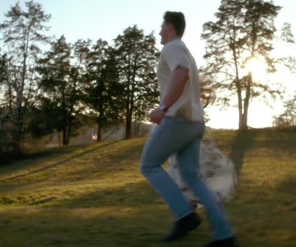 A young couple joyfully runs hand in hand through a grassy field during a beautiful golden hour sunset