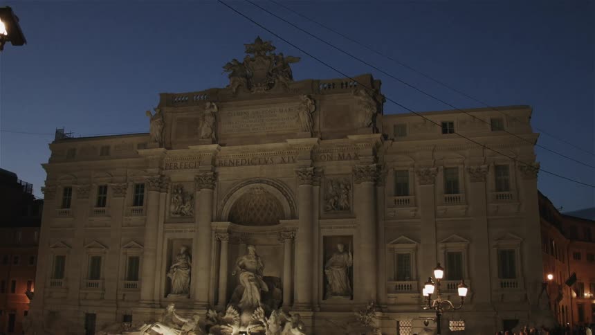 A crowd gathers around a building with statues and pillars