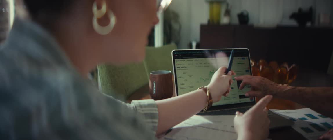 Over the shoulder shot of a woman pointing to a rising financial graph on a laptop screen while in a meeting