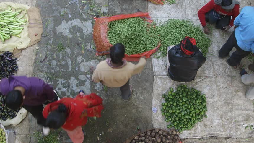 People walking past groups of vegetables on the ground