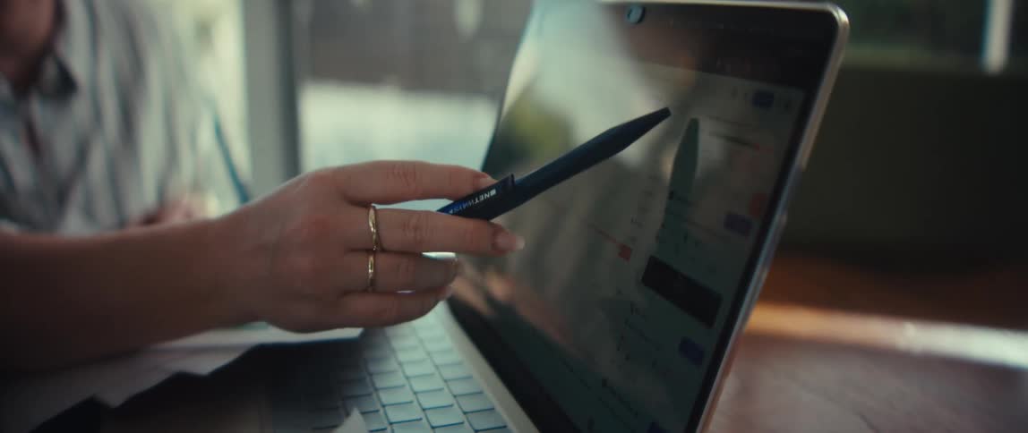 Close-up shot of a woman's hand using a pen to point at financial charts and data analytics on a laptop screen during a business presentation