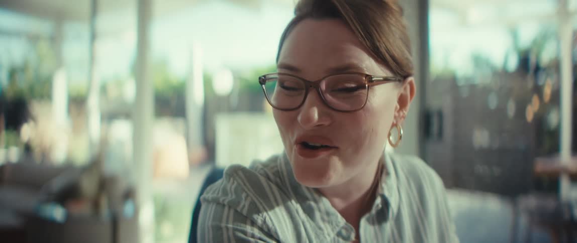 A young woman happily explains financial data on a laptop to a smiling elderly woman in a modern, sunlit home