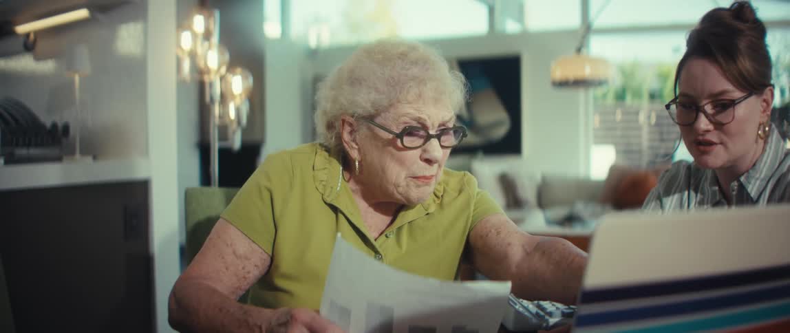 A young woman helps an elderly woman manage her finances on a laptop in a modern home