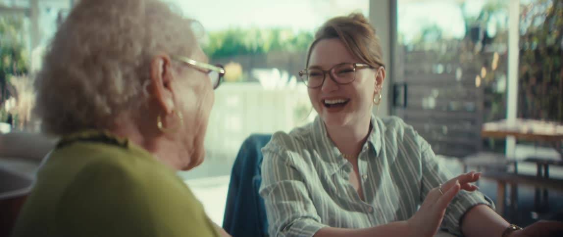 A young woman and a senior woman share a joyful laugh while reviewing finances together at a dining table in a sunlit modern home