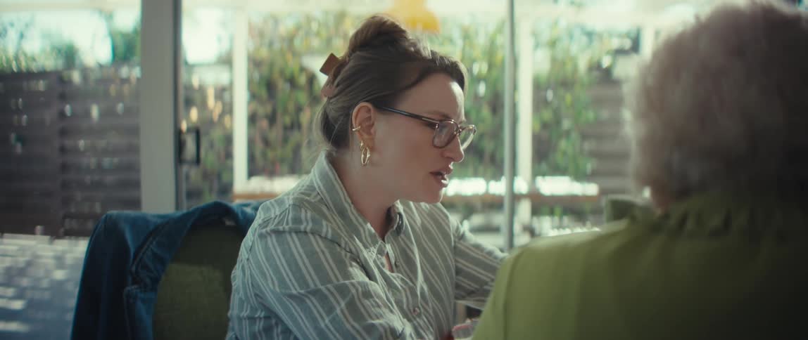 A caring young female advisor with glasses animatedly explains a concept to a senior woman in a brightly lit room