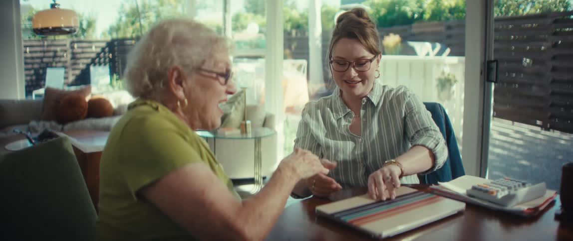 A young professional woman shakes hands with a senior client at her dining table, sealing an agreement during a friendly consultation at home