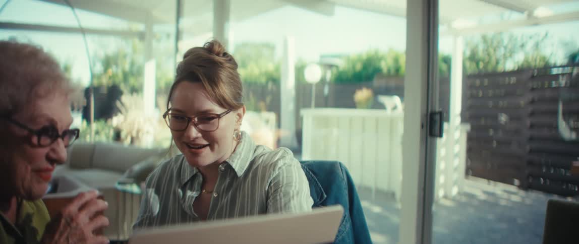 A young financial advisor and her senior client happily shake hands, sealing a deal during a meeting in a bright, modern home