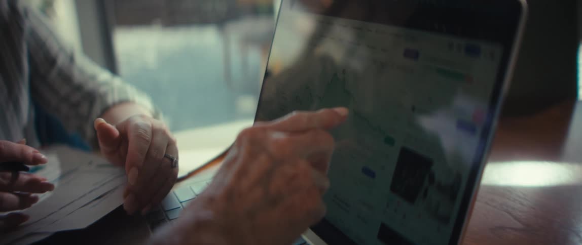 A compassionate financial advisor reviews stock market data on a laptop with her elderly client in her bright, modern home
