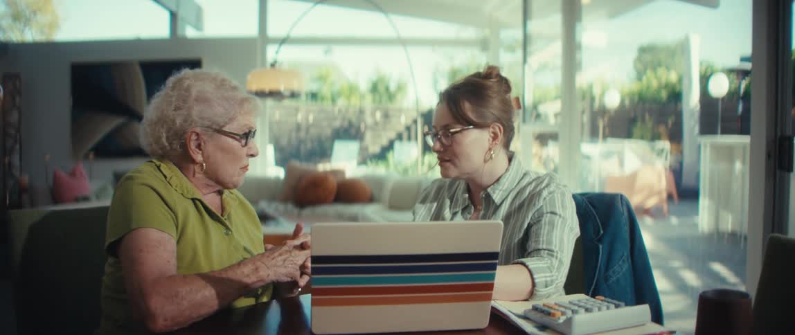 A young woman helps an elderly woman with finances on a laptop during an at-home meeting