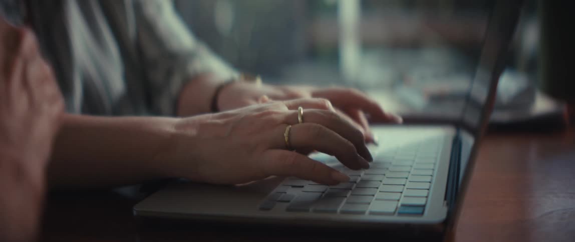 A woman's hands with manicured nails gracefully type on a laptop keyboard in a beautifully lit indoor setting