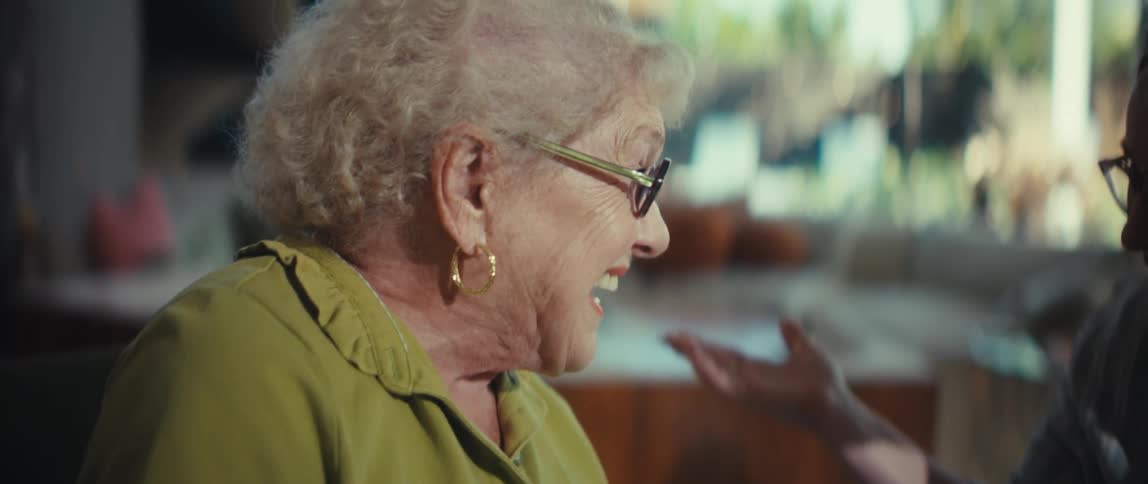 A grandmother and her granddaughter enjoy a heartwarming conversation, smiling and laughing together in a bright, sunlit room