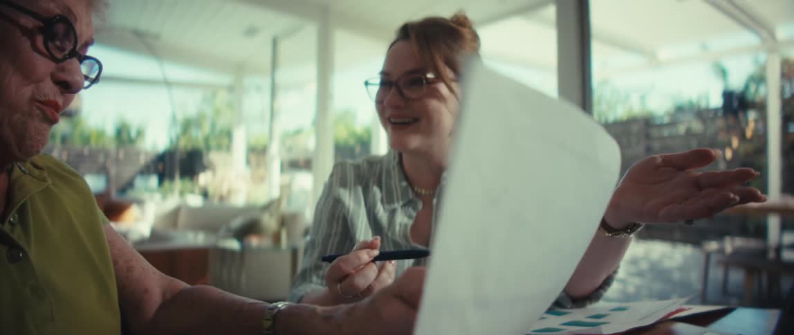 A young financial advisor cheerfully explains a performance chart to her senior client during a meeting in a bright, modern home