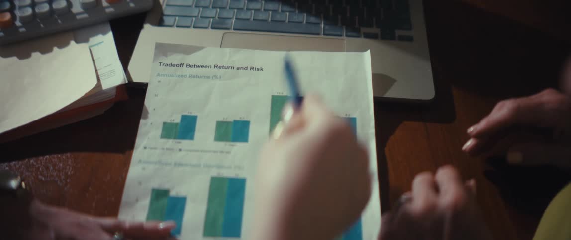 A close-up, top-down view of two colleagues in a meeting analyzing a financial report by pointing a pen at a bar graph