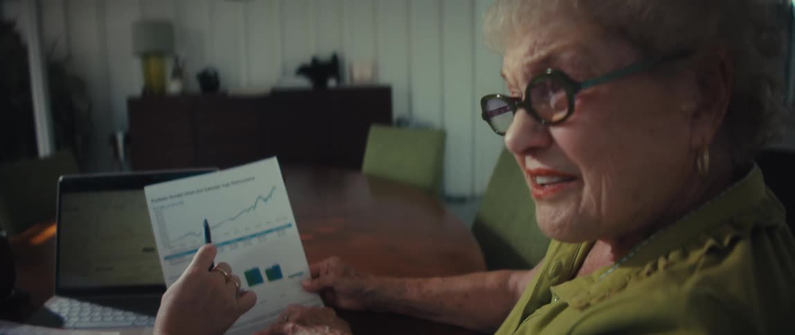 An investment advisor reviews a positive performance chart with an elderly woman at her dining room table