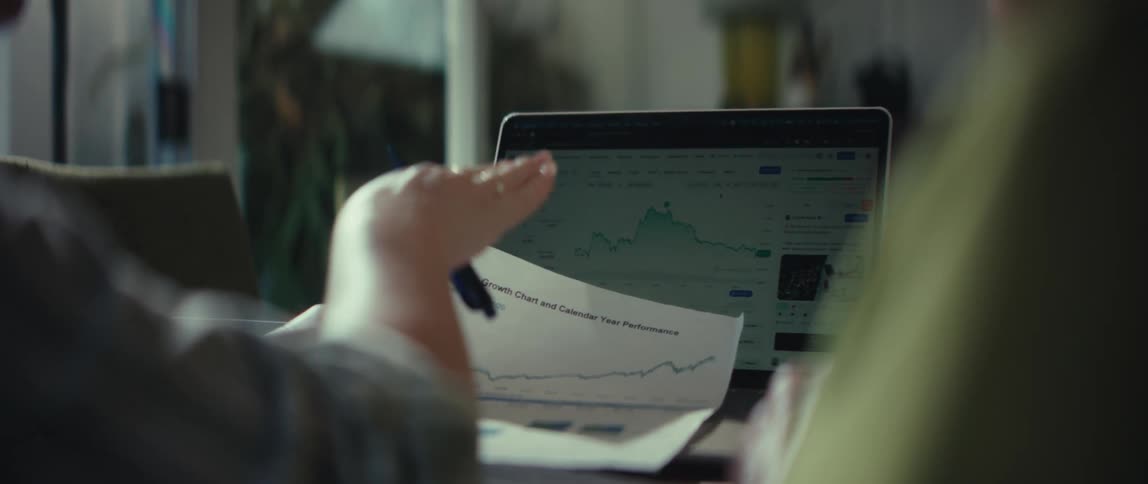 An over-the-shoulder shot of a couple analyzing their financial portfolio's growth on a laptop and printed charts