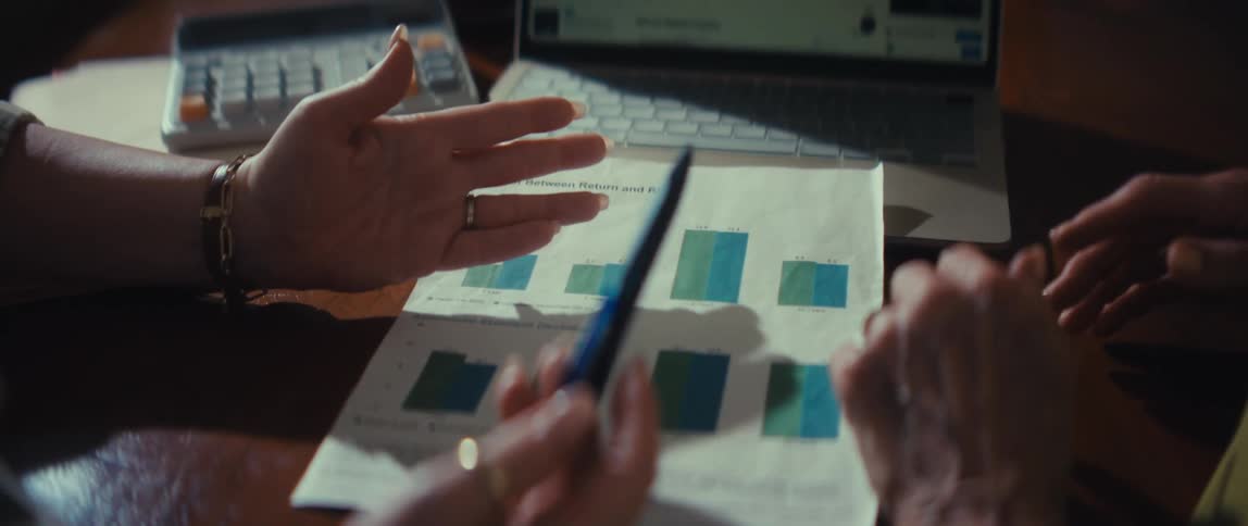 A financial planner explains investment return and risk on a printed bar graph to an elderly client during a consultation
