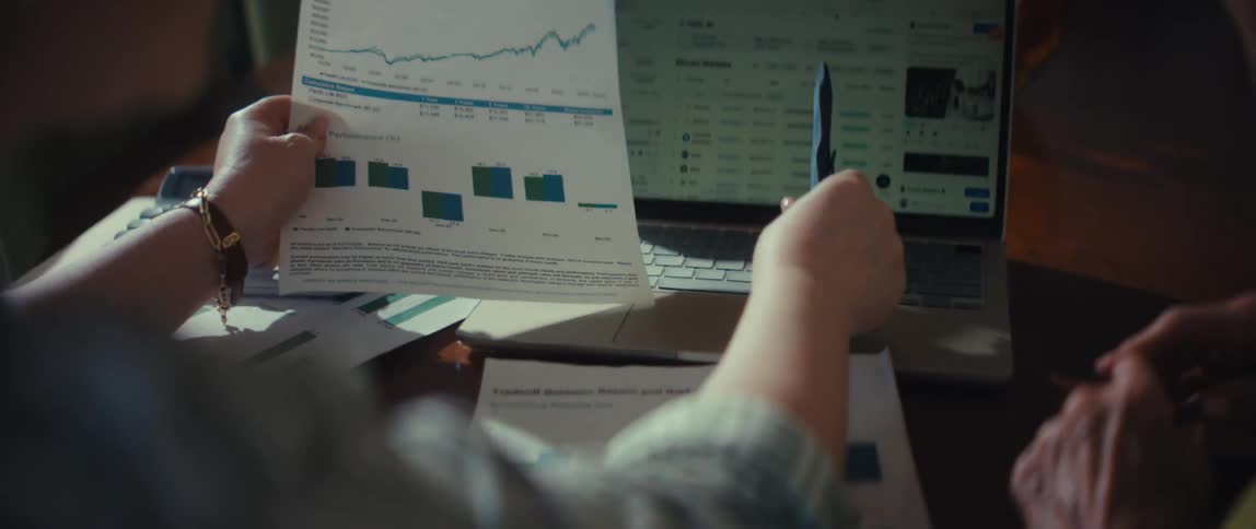 An investor compares their portfolio growth chart on paper to live market data on their laptop while analyzing performance