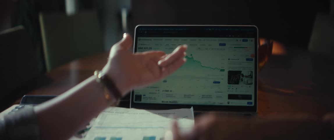 An over-the-shoulder shot of two people reviewing financial charts on a laptop before shaking hands to finalize a deal