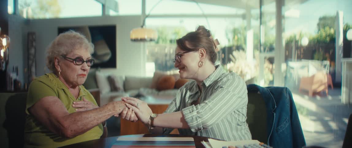 A young woman offers support and comfort to an elderly woman during a serious discussion, concluding with a warm handshake and holding her hand