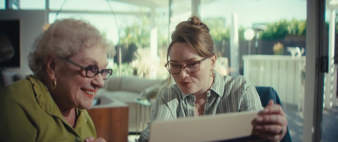 A financial consultant and a senior client smile as they review documents and shake hands on an agreement in a bright modern home