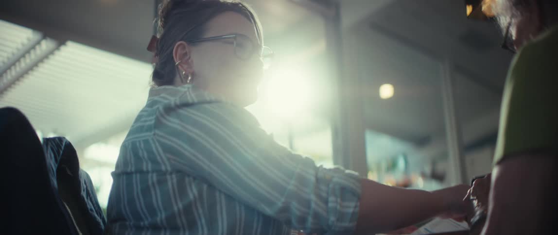 A professional woman with glasses and her hair up explains a chart during a sunlit meeting