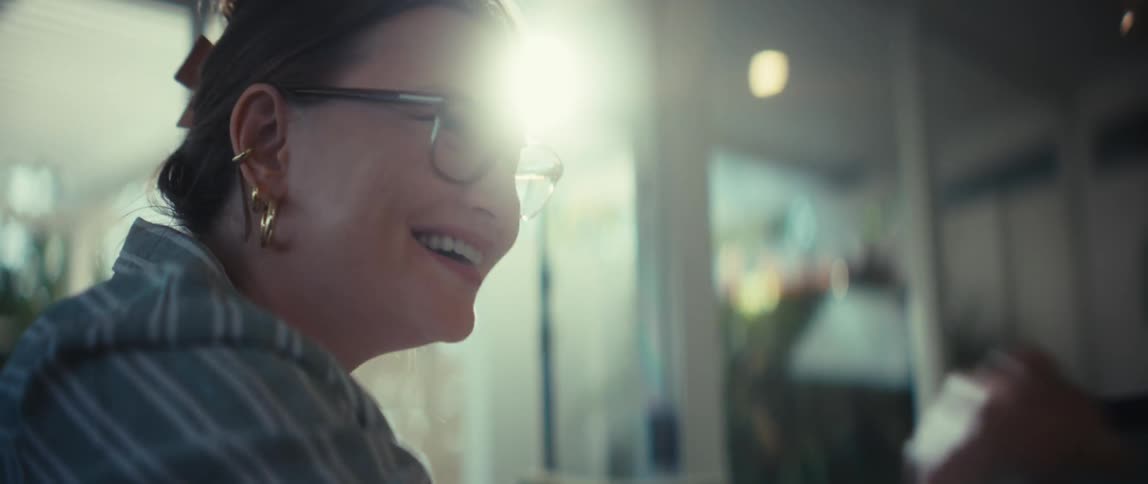 A happy young woman with glasses smiles and laughs during a cheerful conversation on a sunny day in slow motion