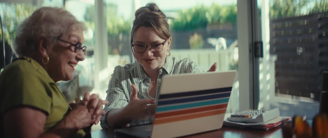 A young financial advisor happily assists an elderly client on her laptop, culminating in a warm handshake