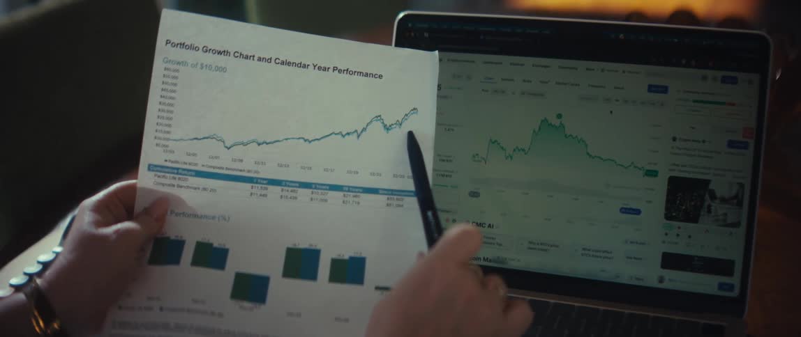 A financial investor analyzes portfolio performance by comparing a printed growth chart with live market data on a laptop