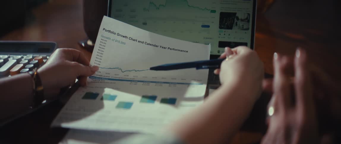An investor compares a printed portfolio growth chart with a live cryptocurrency trading chart on their laptop
