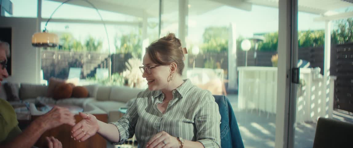 A female financial advisor happily shakes hands with her elderly client after a successful consultation in a bright, modern home