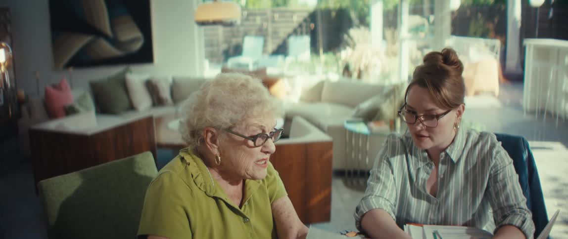 An attentive young woman explains paperwork and financial documents to an elderly woman in her modern home