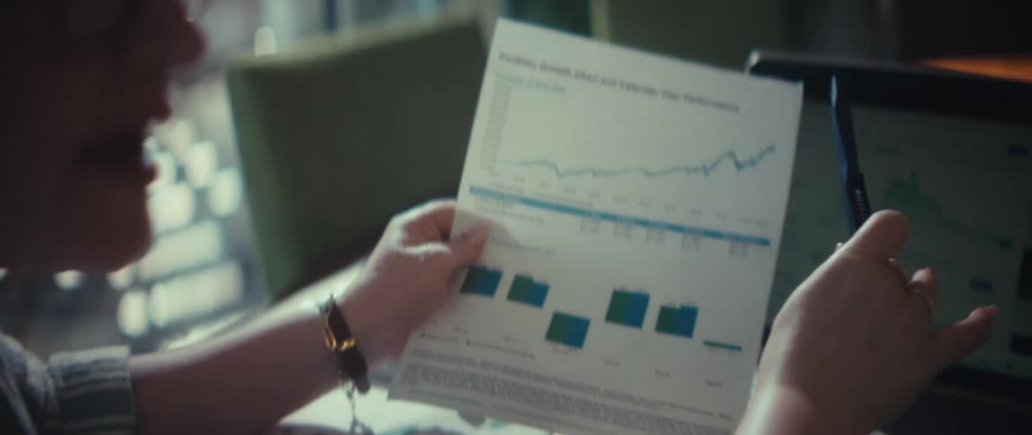 Financial advisor explains investment performance charts on a laptop and printed report to an elderly client