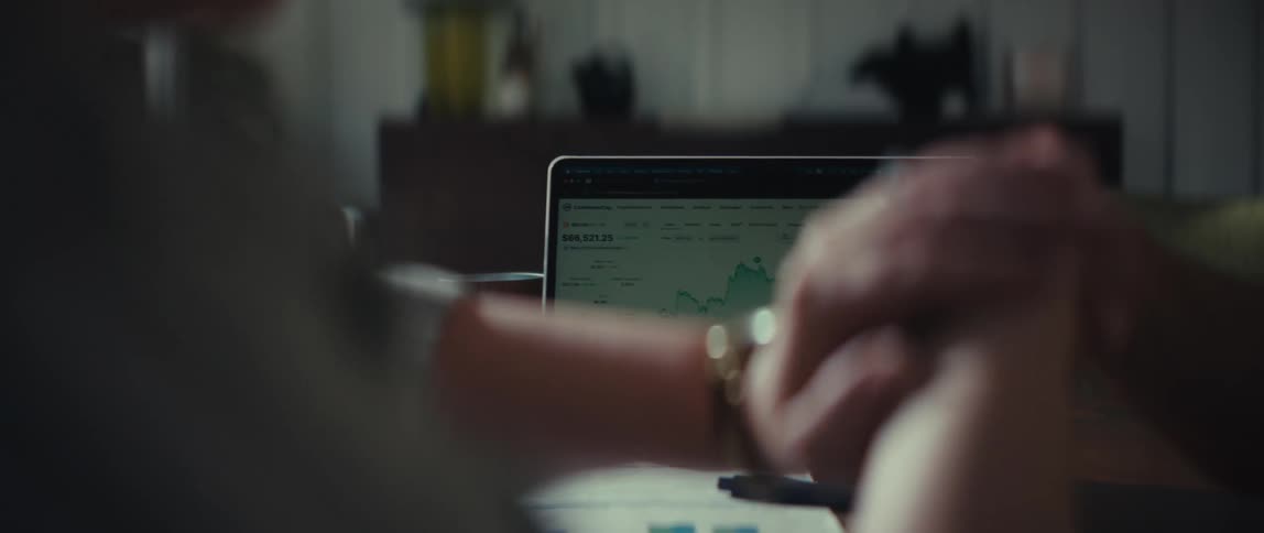 An over-the-shoulder view shows a person analyzing a financial chart on a laptop at their desk