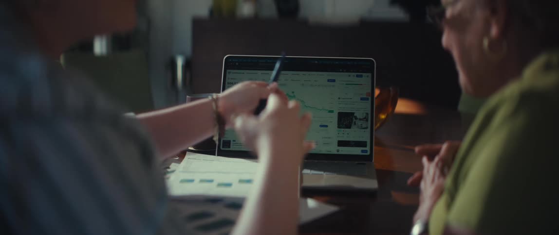 A financial advisor explains stock market data to a senior client on a laptop before holding her hand in reassurance