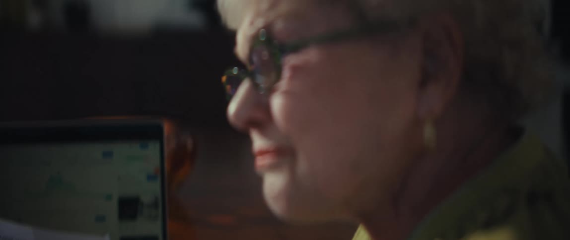An elderly couple analyzes their financial investments by reviewing cryptocurrency charts on a laptop and printed portfolio reports