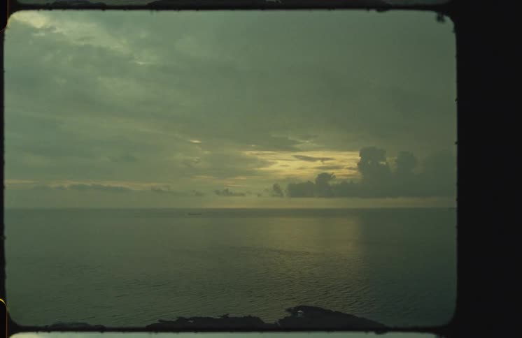 Vintage 8mm film captures a moody, overcast seascape at sunrise with a lone ship on the distant horizon